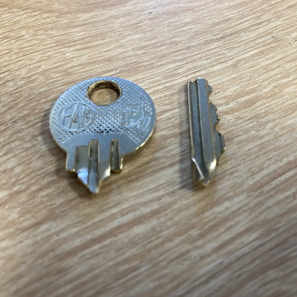 Een sleutel die in twee stukken is afgebroken, naast elkaar op een houten tafel